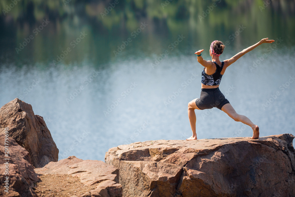 年轻女子在岩石上的晨间公园里做瑜伽，湖景优美。瑜伽女孩