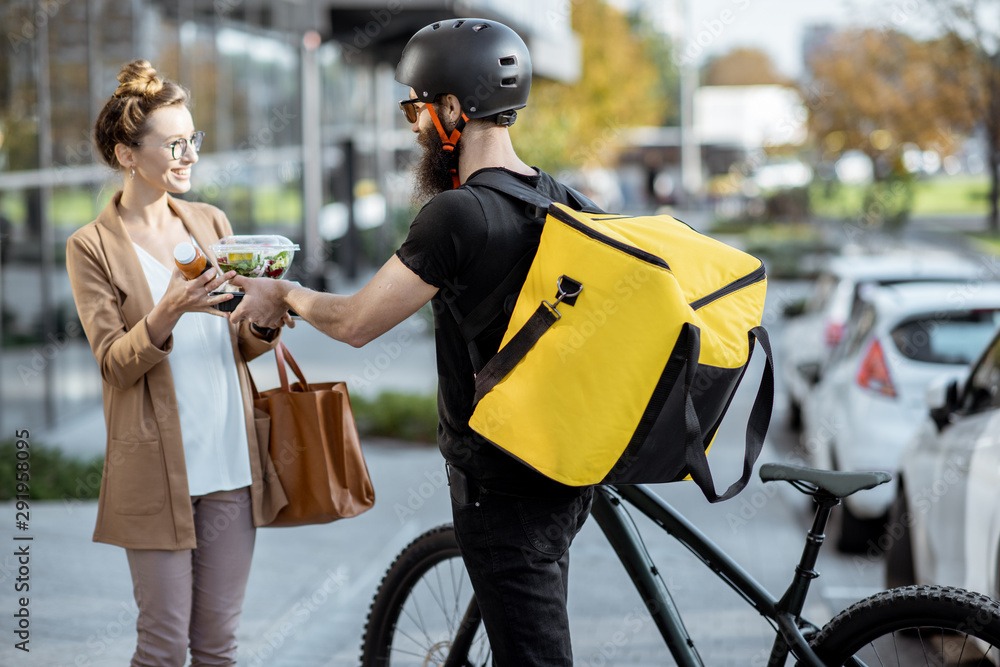 Courier delivering fresh lunches to a young business woman on a bicycle with thermal backpack. Takea