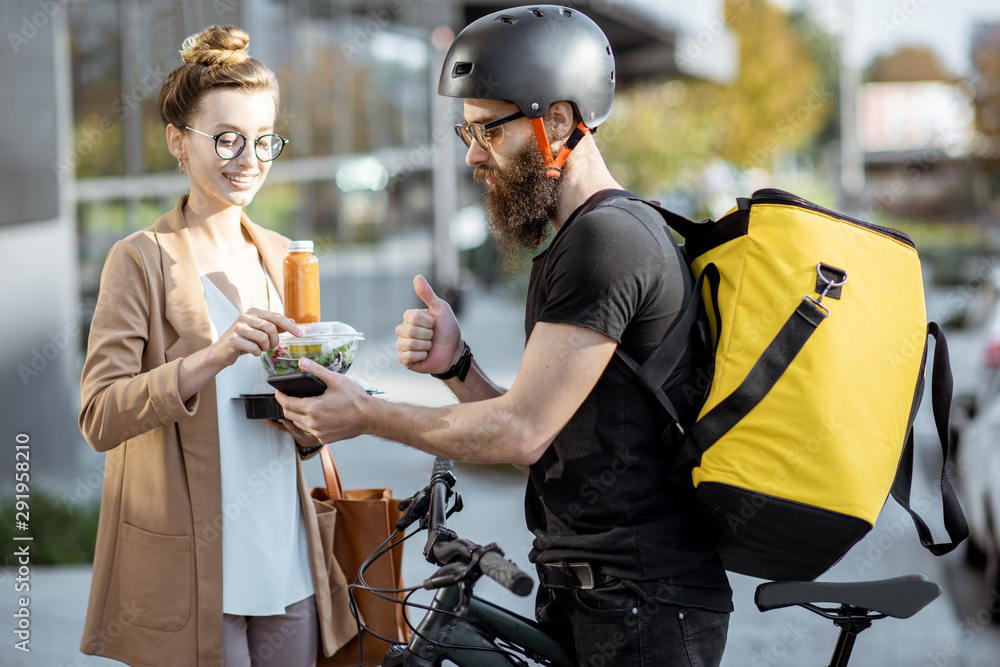 快递员用热背包骑自行车给一位年轻的商务女性送新鲜午餐。Takea