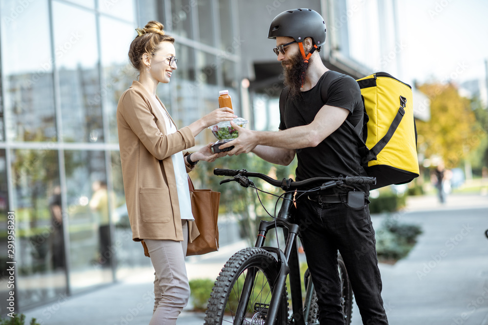 Courier delivering fresh lunches to a young business woman on a bicycle with thermal backpack. Takea