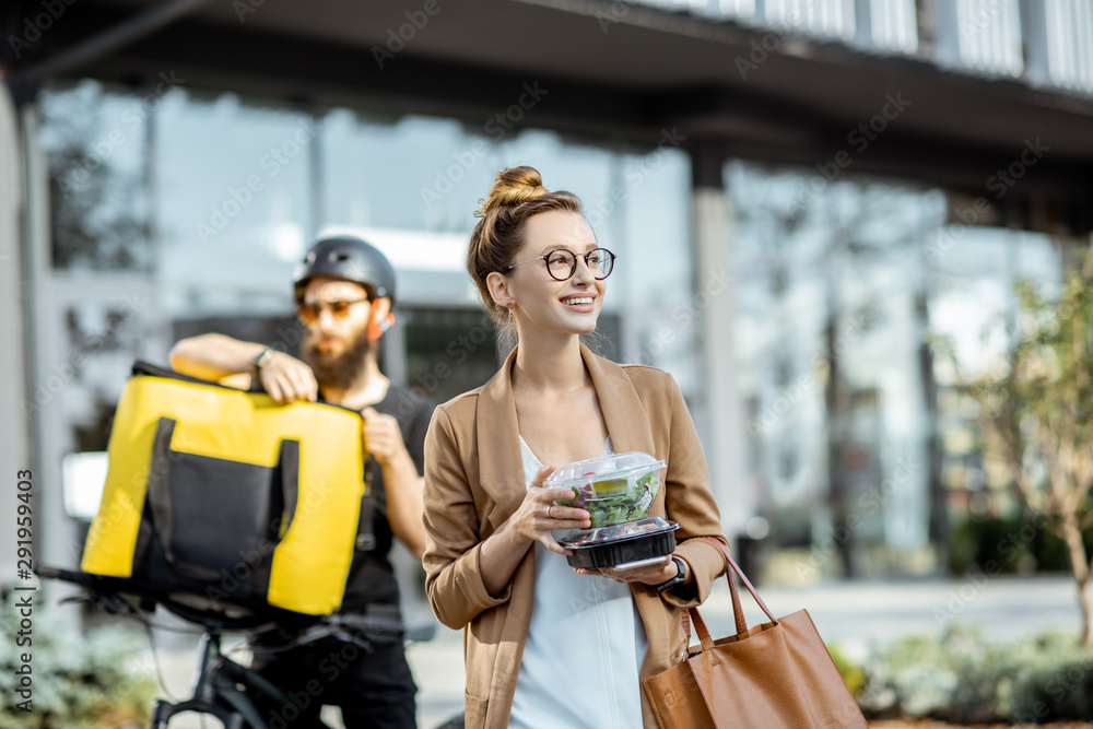 Happy businesswoman receiving fresh takaway lunches, standing near the office building with a male c