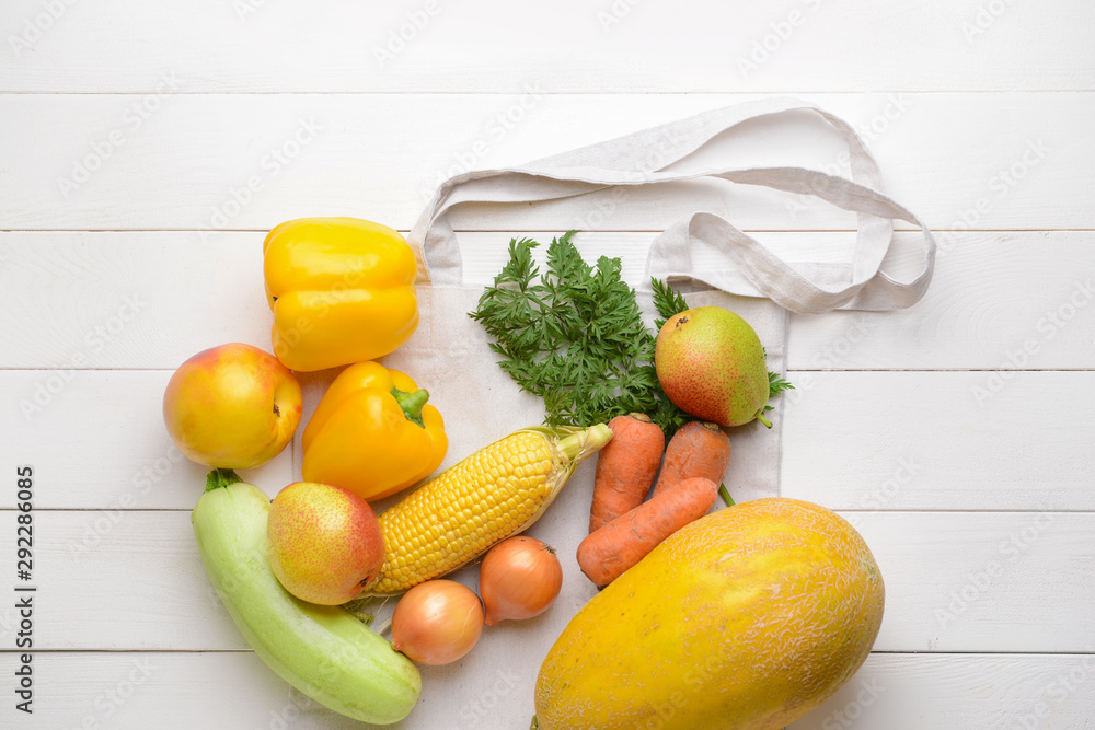 白色木质背景上有许多健康蔬菜和水果的购物袋