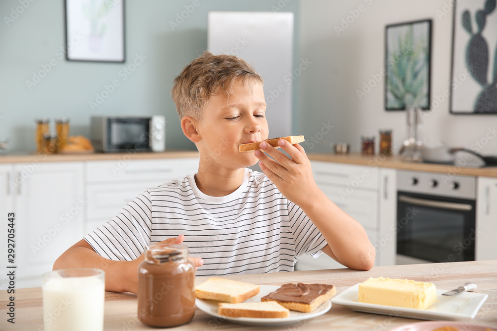 有趣的小男孩在厨房里吃着美味的烤面包和巧克力