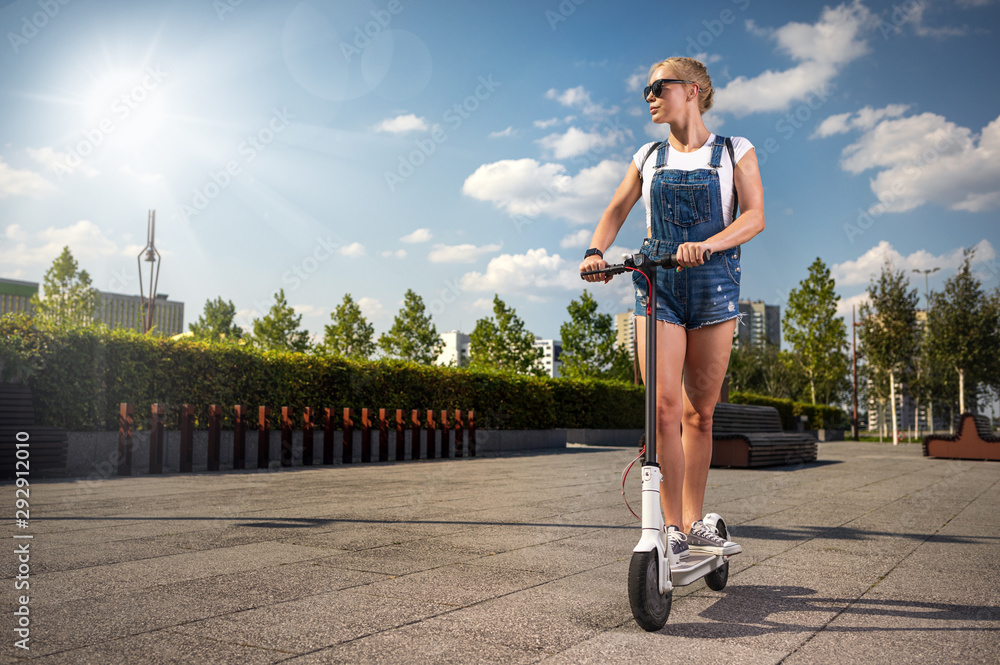 城市里阳光明媚的日子里骑着电动滑板车的时髦女人
