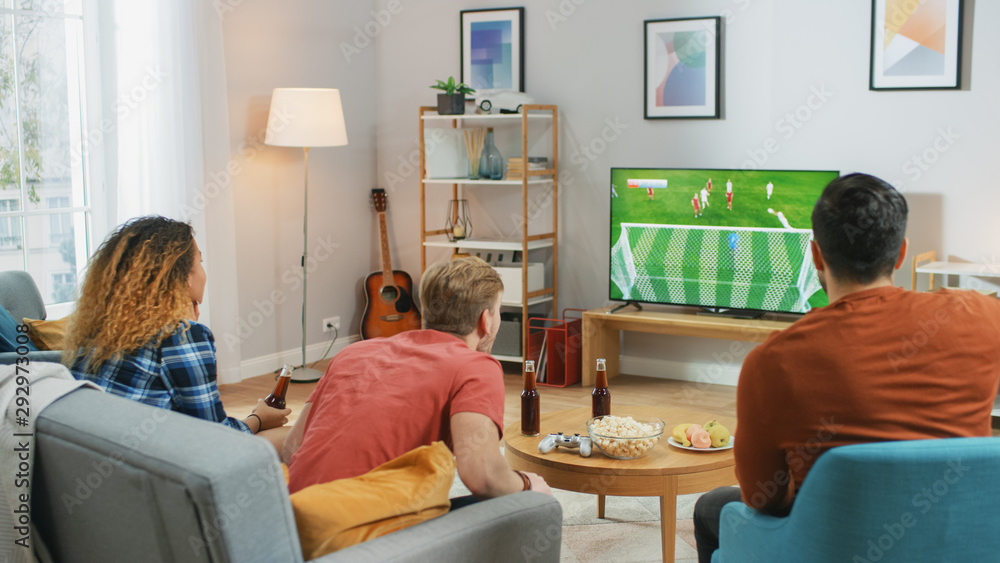 三名体育迷坐在客厅的沙发上观看电视上的重要足球比赛，欢呼
