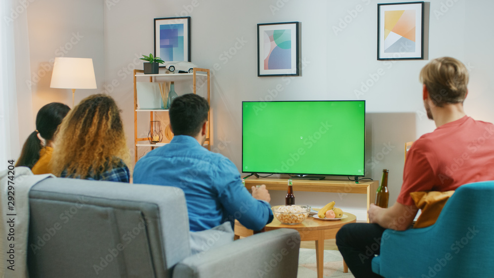 快乐的朋友们坐在家里看绿色Chroma键屏幕，在沙发上放松。看运动