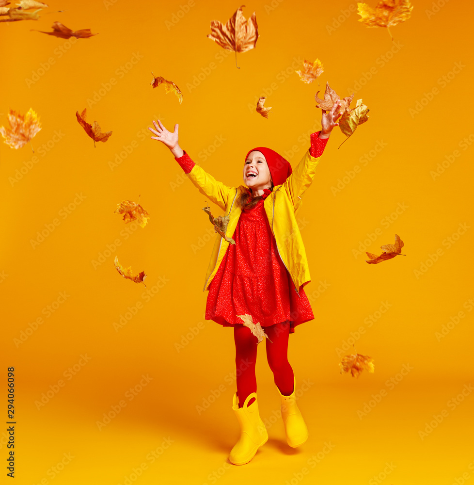 快乐的情绪开朗的小女孩在彩色黄色的bac上与秋叶一起跳跃和大笑