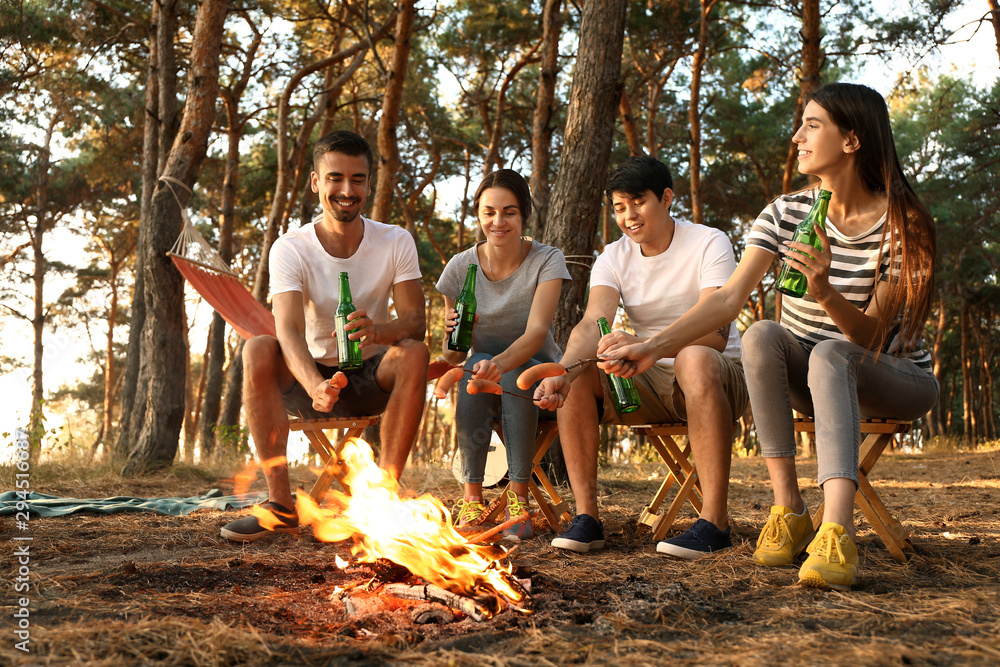 年轻的朋友们在篝火上烤香肠，在营地喝啤酒