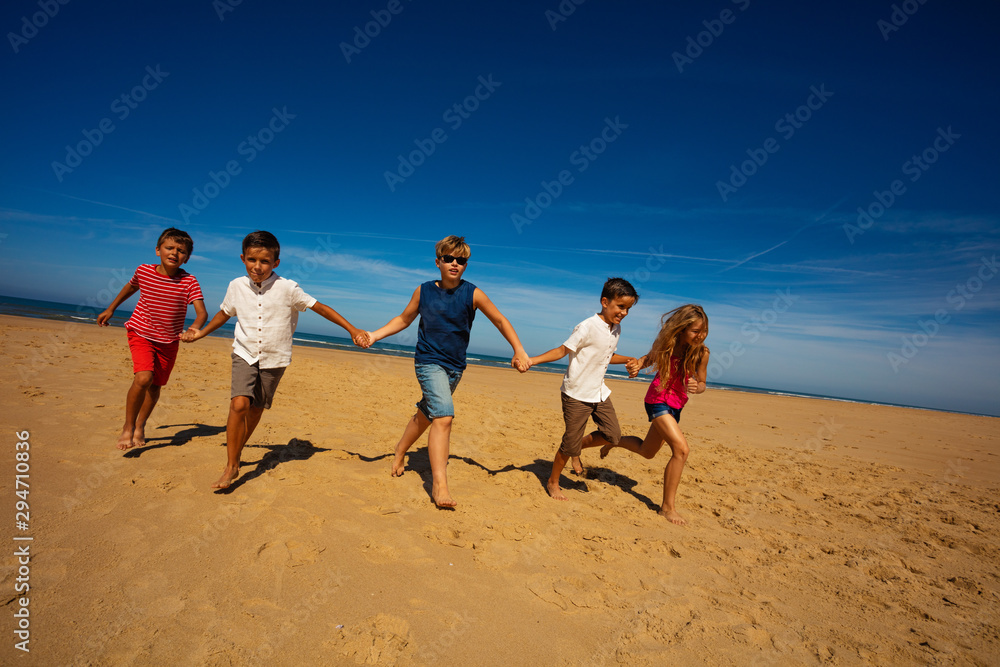 Group of kids run holding hands on the sand beach
