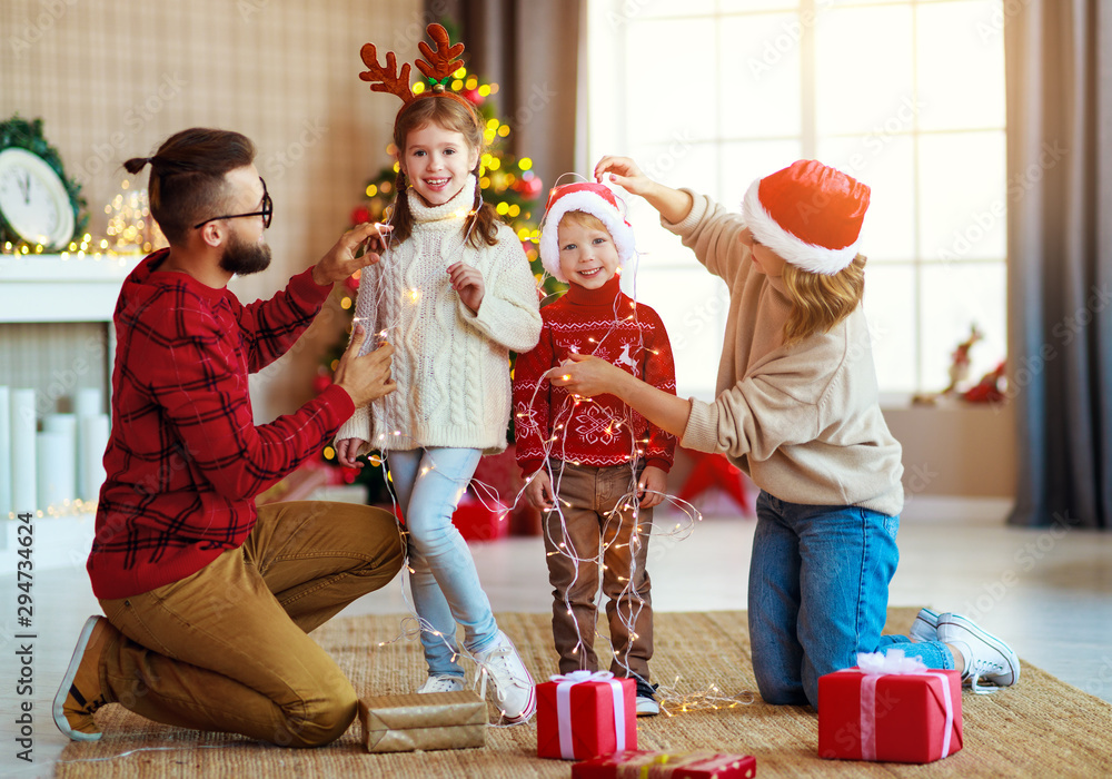 幸福的家庭装饰圣诞树，父母带着花环和孩子们玩耍。
