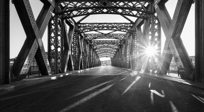 在一个阳光明媚的日子里，黑色和白色的沥青路面下的钢结构桥梁在城市。电动汽车