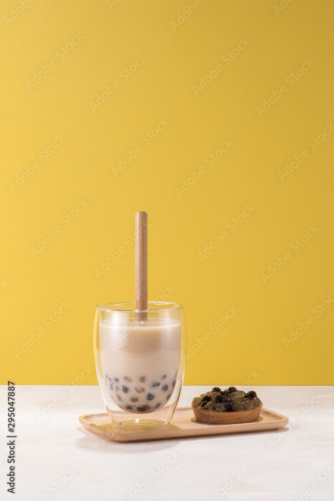 一杯珍珠奶茶（也称为气泡茶）和一盘黄色背景上的木薯球
