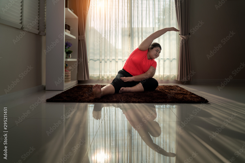 亚洲超重女性锻炼瑜伽独自坐在家里的地板上做侧弯姿势，瑜伽冥想