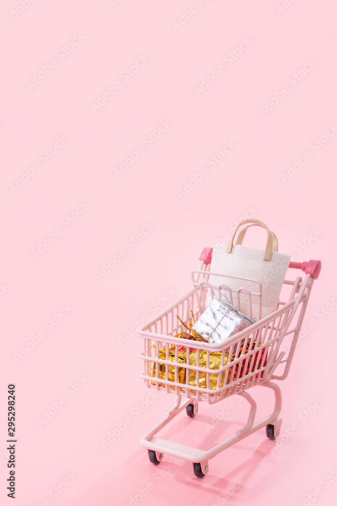 年度大减价购物季概念-迷你粉色购物车手推车，装满纸袋礼物隔离打开