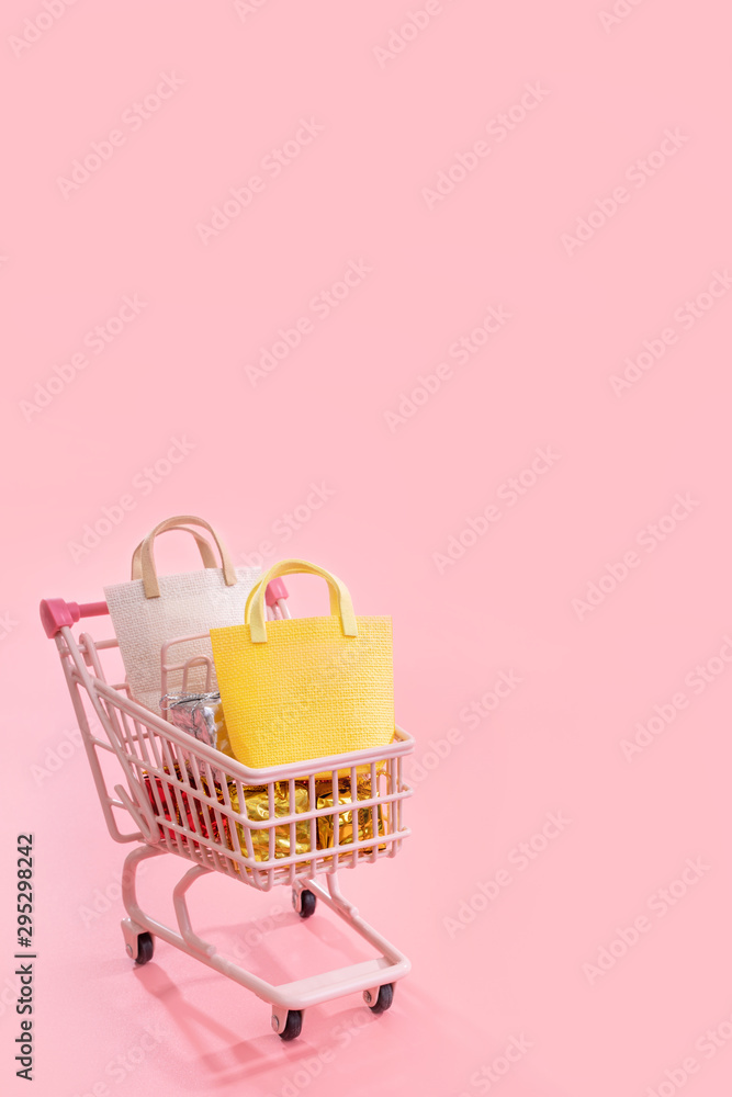 年度大减价购物季概念-迷你粉色购物车手推车，装满纸袋礼物隔离开