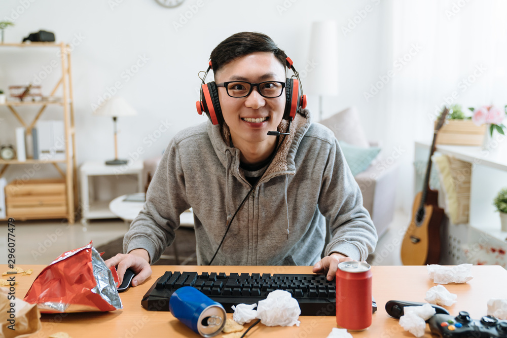 专注的男性玩家微笑着看着游戏，在堆满垃圾的桌子上使用电脑键盘。con