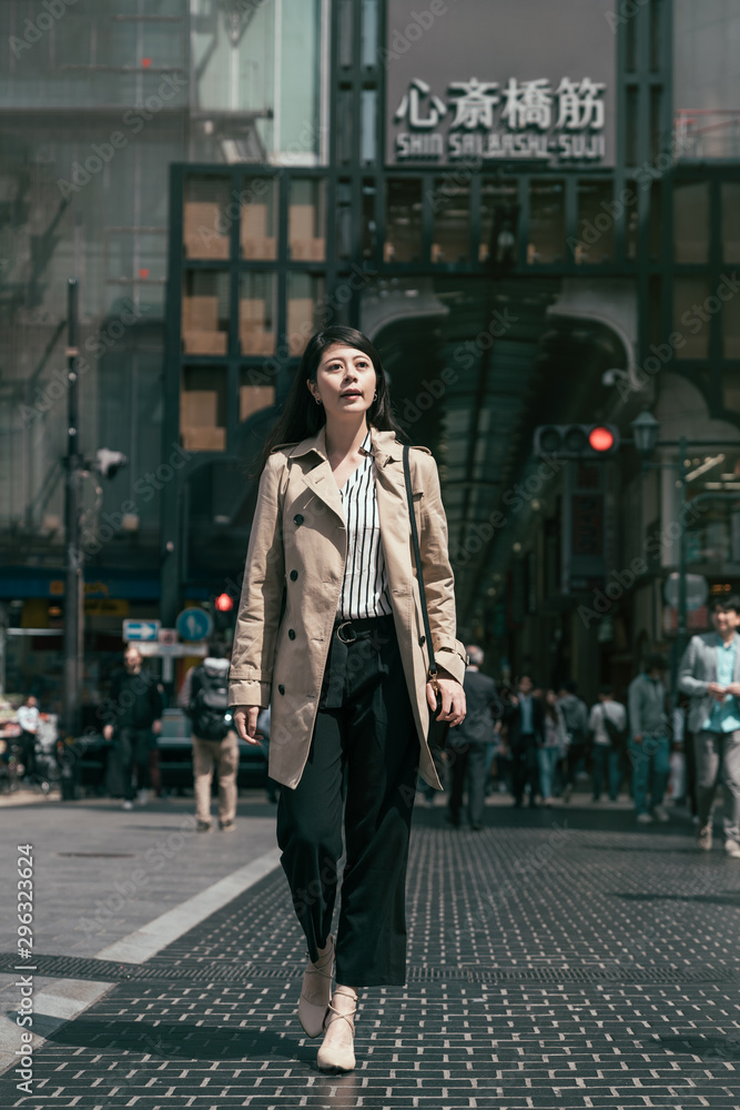 年轻漂亮的亚洲女工穿着米色外套，带着袋子走在新赛桥的秋天街道上