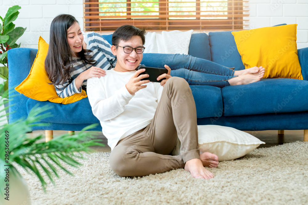 幸福的亚洲新婚夫妇一起在客厅玩智能手机游戏