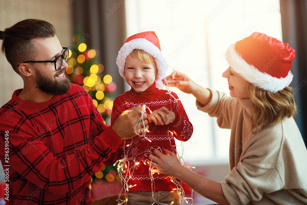 幸福的家庭装饰圣诞树，父母带着花环和小儿子玩耍
