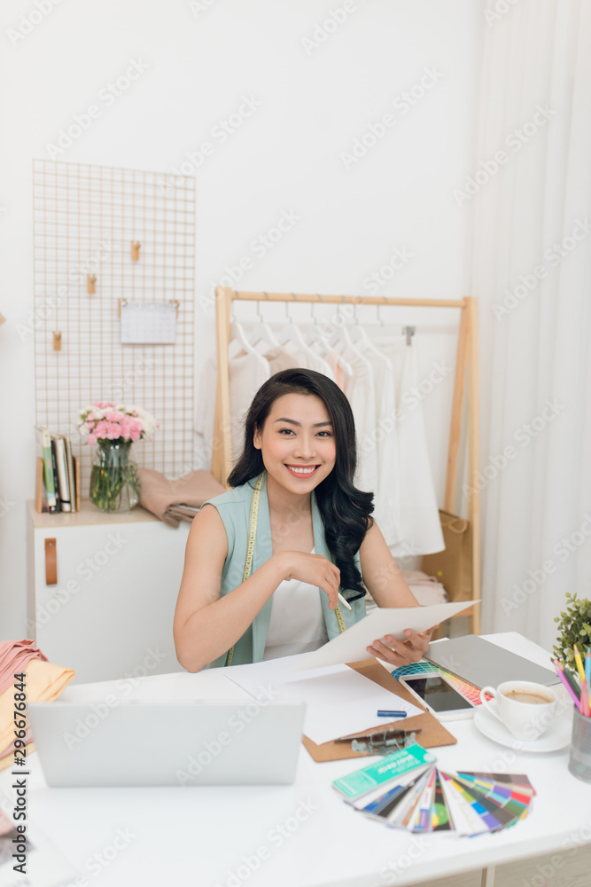 Fashion designer at work. Happy young Asian woman drawing while sitting at her working place in fash