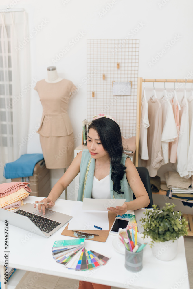 Pretty young casual businesswoman sitting in front of laptop in workshop or studio and searching for