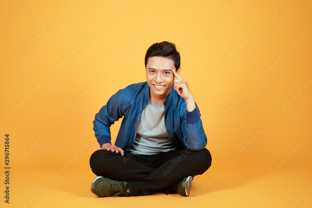 年轻休闲的亚洲男子盘腿坐着，抱着头，对着镜头微笑。i