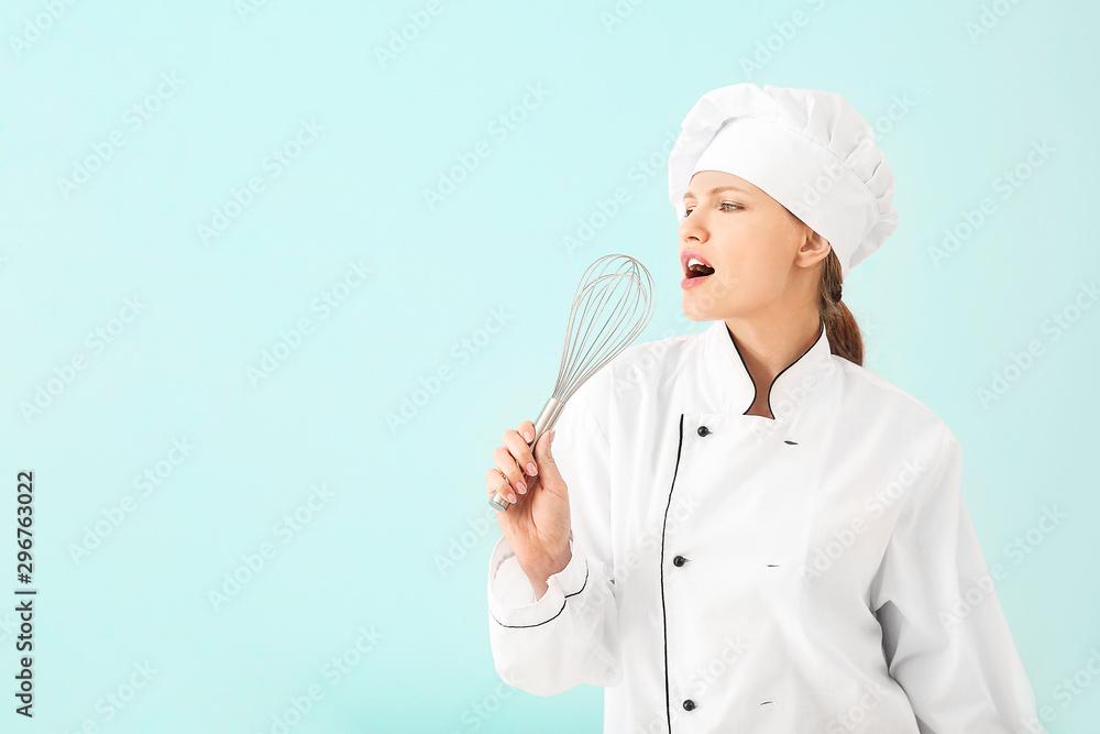Beautiful female chef using whisk as microphone for singing on light background