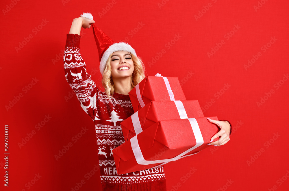 快乐快乐的年轻女孩戴着圣诞帽，拿着红底礼物，笑着跳了起来。