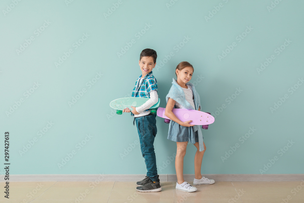 可爱的时尚儿童在彩色墙附近玩滑板