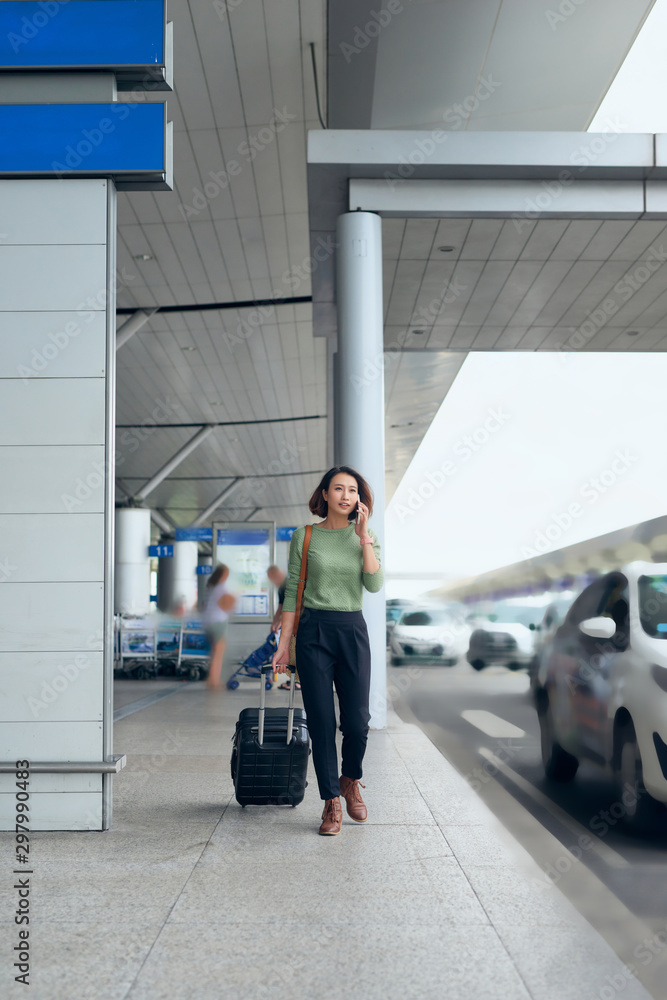 Smiling pretty girl using mobile phone and looking into distance. Lady with suitcase concept