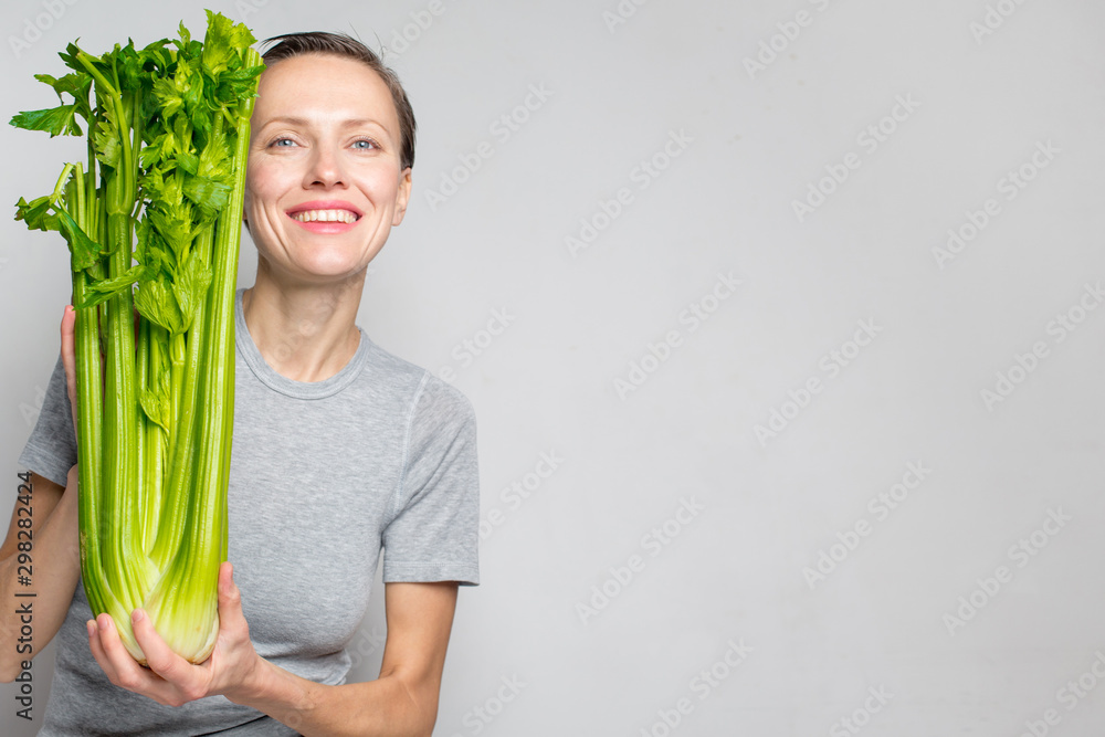拿着绿色新鲜芹菜的女人。健康饮食、素食、节食和以人为本