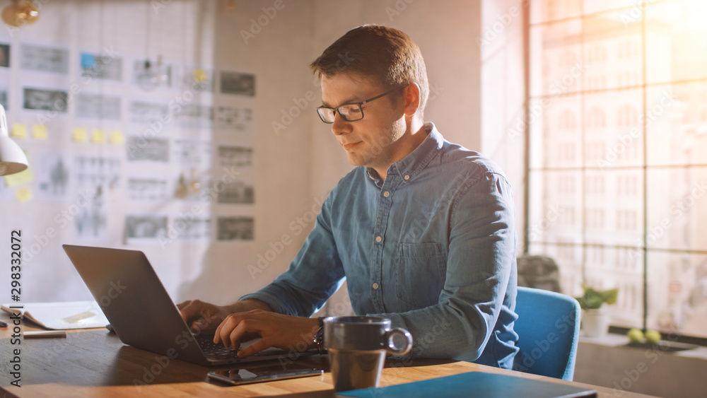专业创意男人坐在家庭办公室工作室的桌子旁用笔记本电脑工作。男人在工作