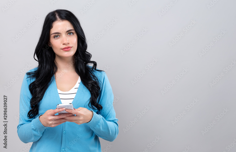 年轻女子在灰色背景下使用手机