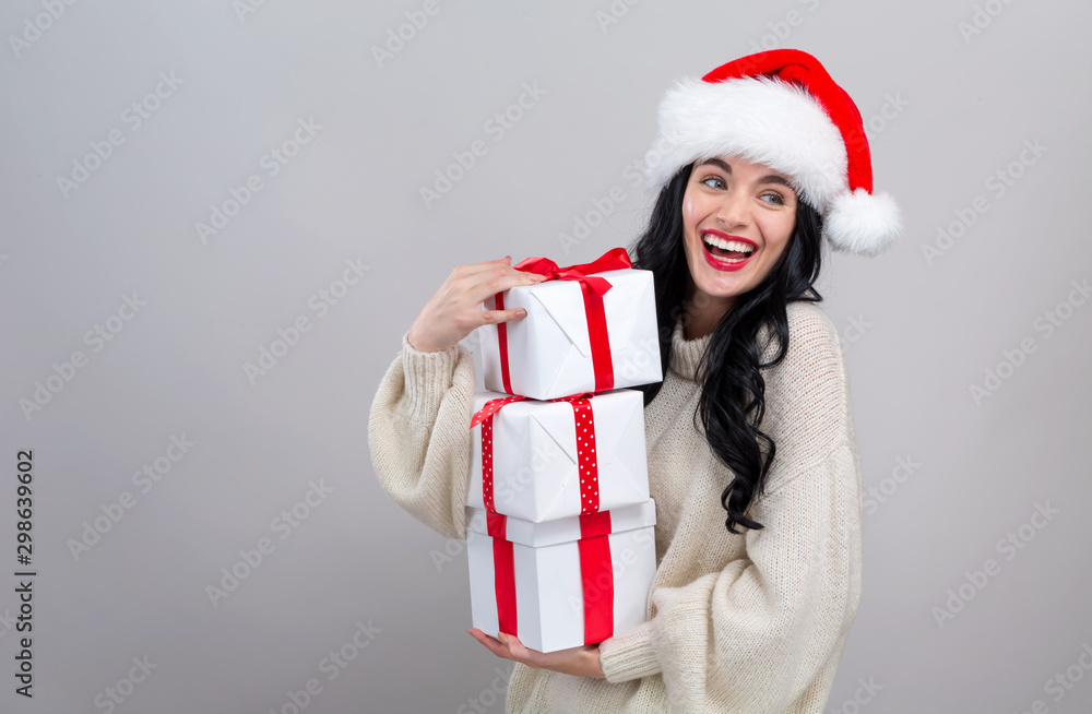 戴着圣诞老人帽的年轻女子拿着灰色背景的礼盒