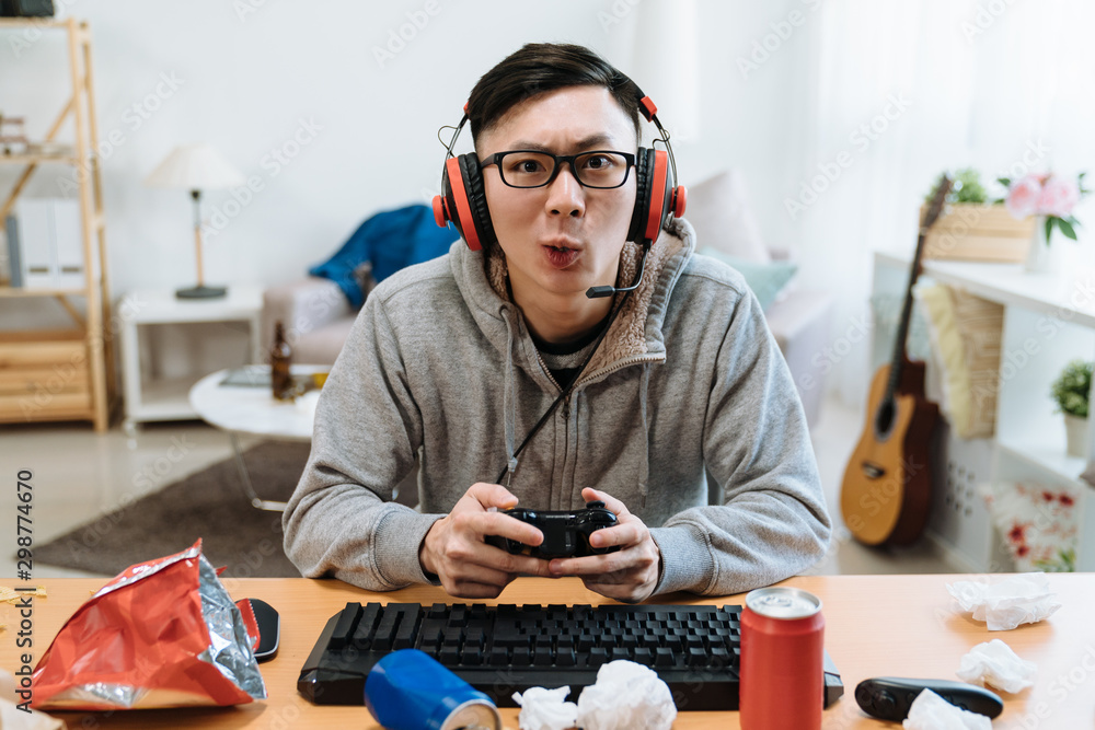 在视频游戏机上玩游戏的Nerd geek年轻成年男子喜欢网络游戏。亚洲男性玩家集中注意力