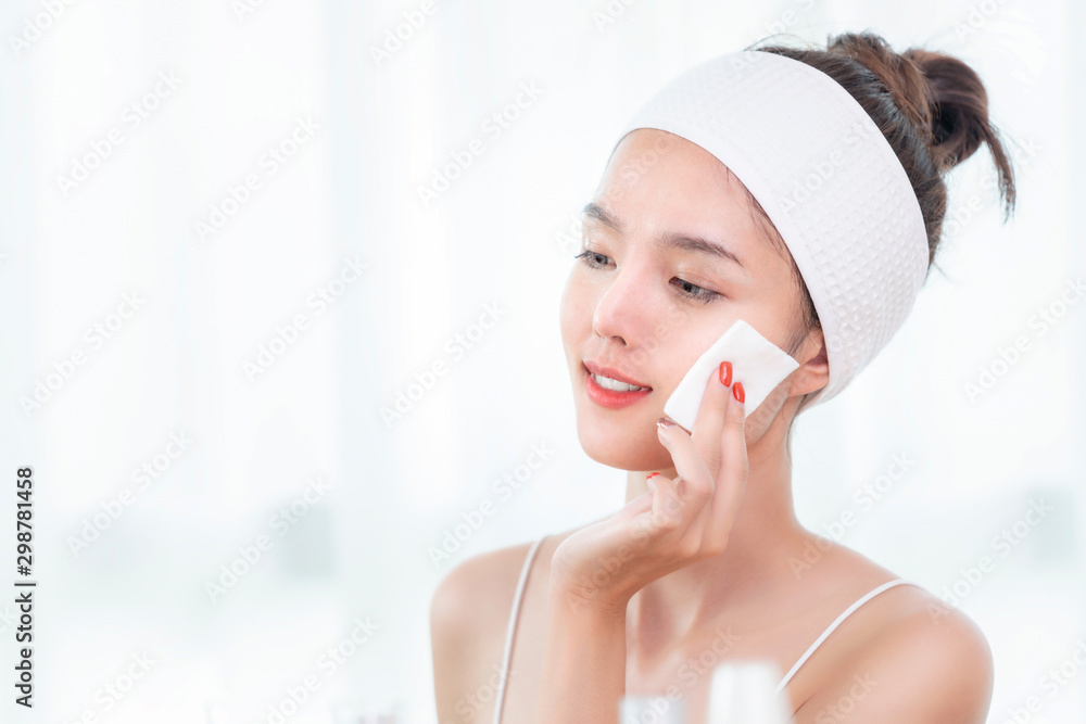 亚洲女孩在浴室里用乳液和棉花去除脸上的化妆品
