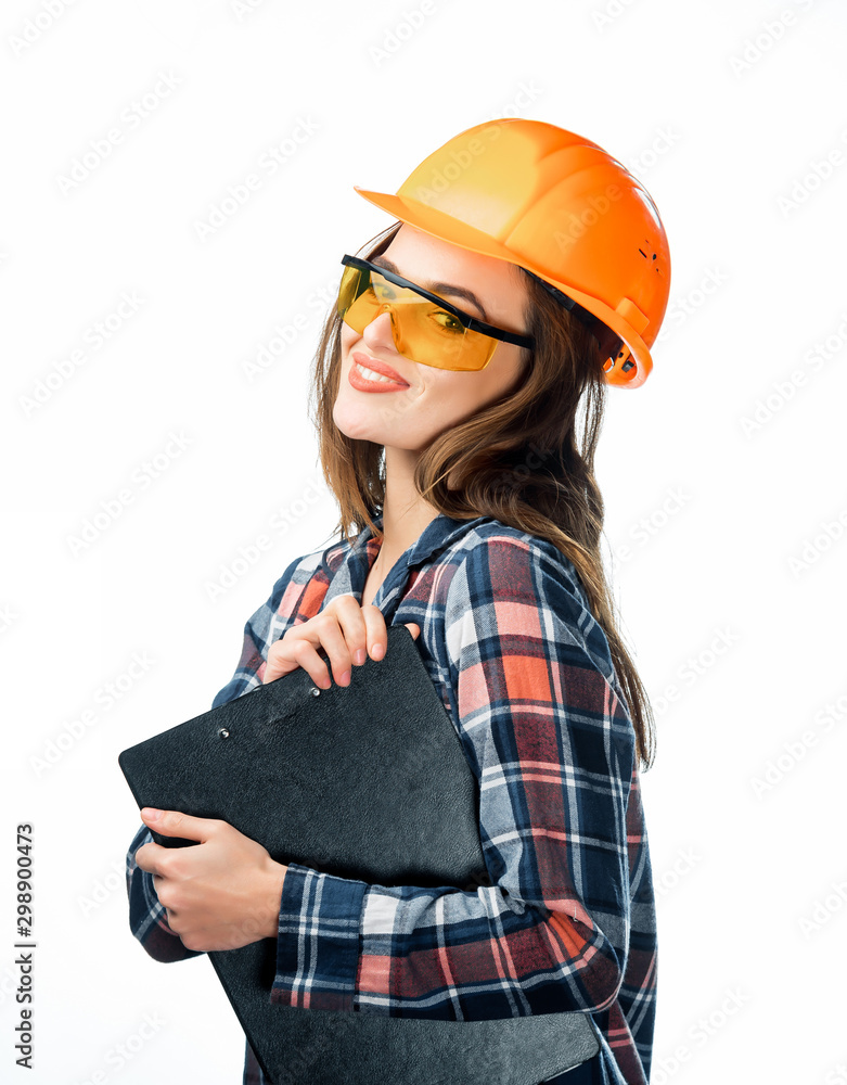 快乐的年轻女子戴着橙色安全帽，戴着黄色眼镜，穿着格子衬衫，手里拿着一个夹子