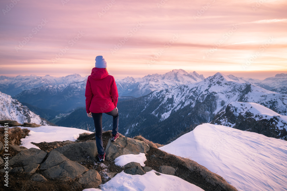 Young woman in snowy mountains at sunset in winter. Beautiful slim girl on the mountain peak against