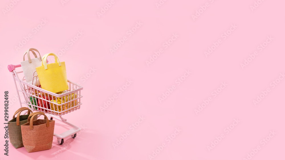 年度大减价购物季概念-迷你粉色购物车手推车，装满纸袋，隔离在上面