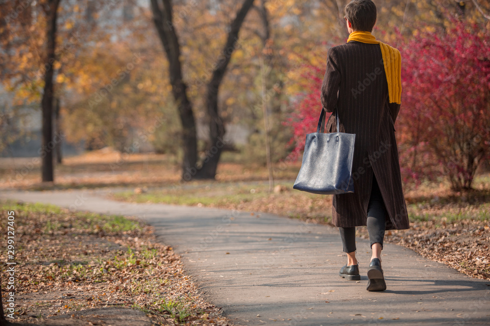 穿着时尚秋季服装的时尚秋季女性在秋季公园散步