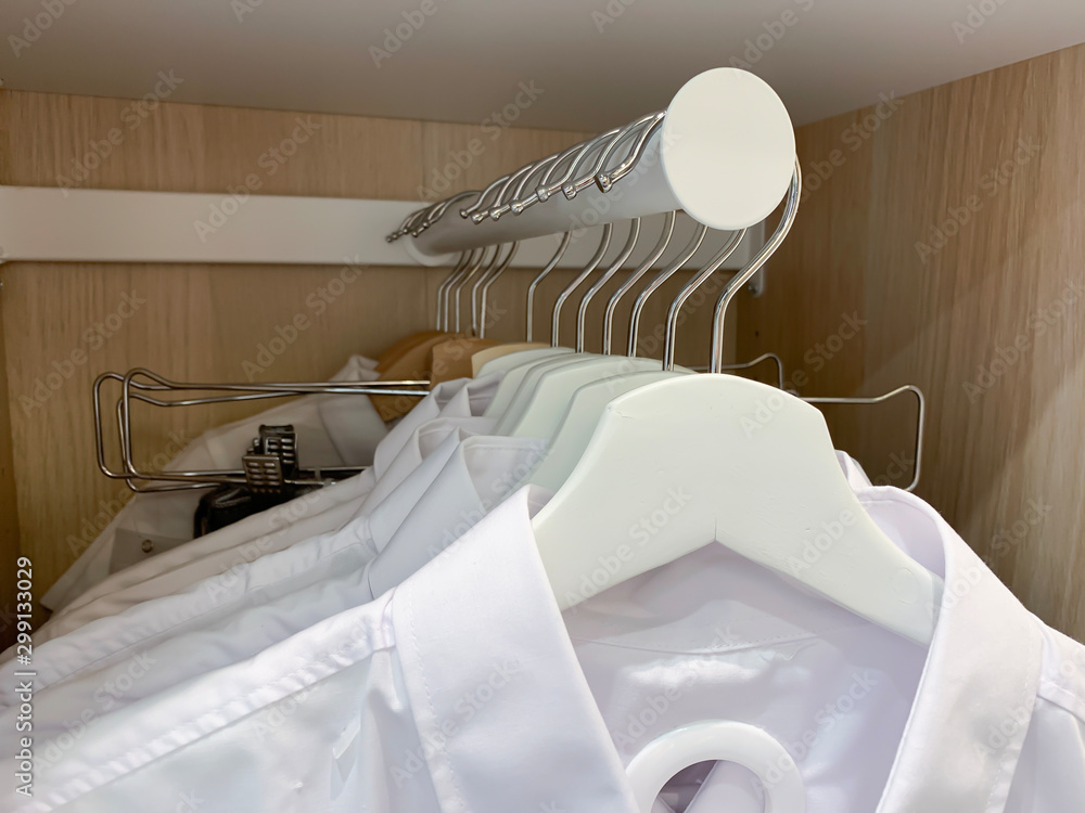 衣柜里挂在白色木制衣架上的许多棉质休闲男士衬衫