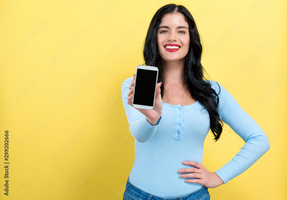 一名年轻女子在黄色背景下手里拿着一部手机