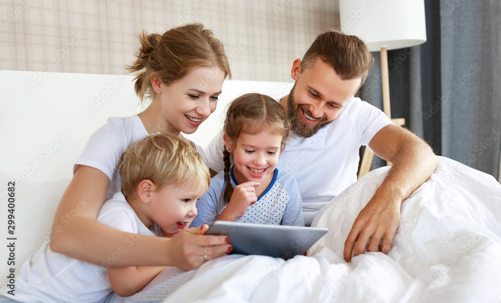 幸福的一家人在家里的床上用平板电脑开怀大笑。看电影和上网。
