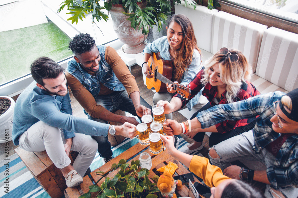 Group of multiracial people having fun toasting beer and playing guitar laughing together