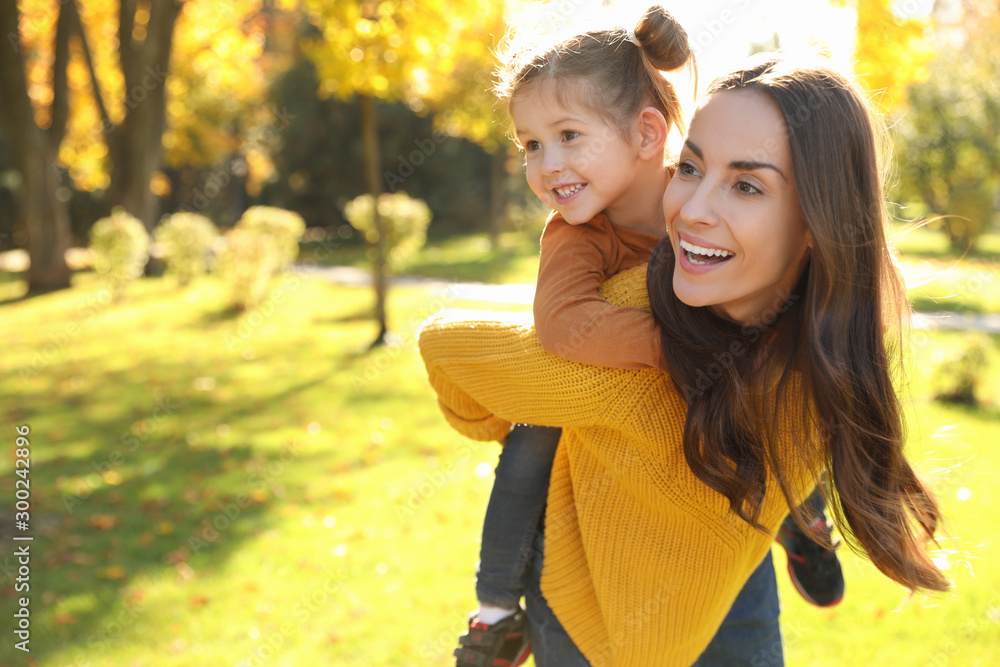 快乐的女人带着小女儿在阳光明媚的公园里。秋天散步