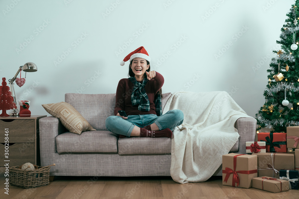 电视圣诞节目假日休闲概念。微笑的女人坐在沙发上，拿着电视遥控器