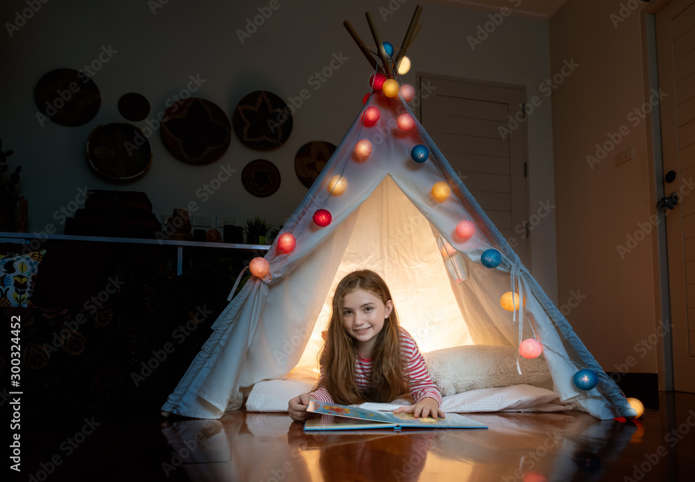 Attractive cute girl lying and reading book inside tepee tent in her bedroom enjoy happy time.