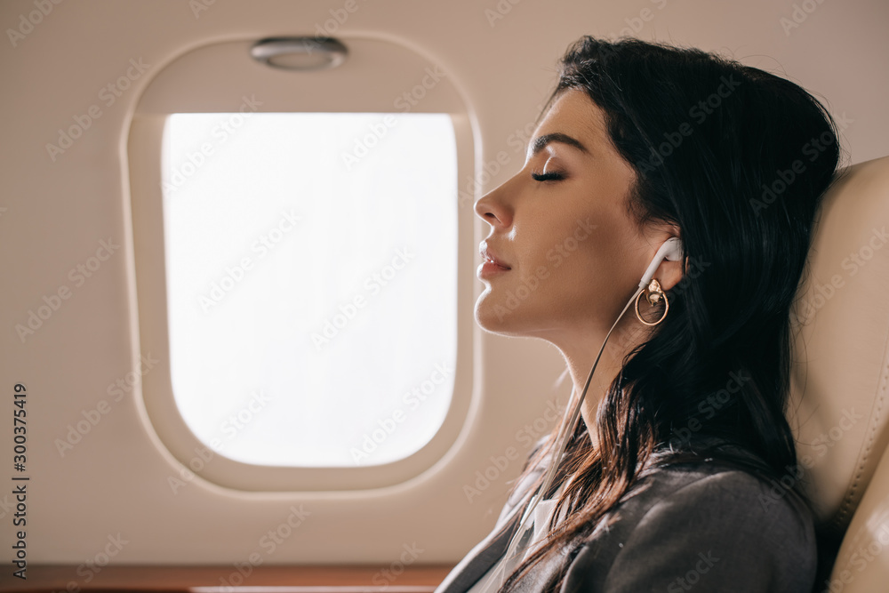 迷人的女商人闭着眼睛在私人飞机上听音乐的侧视图