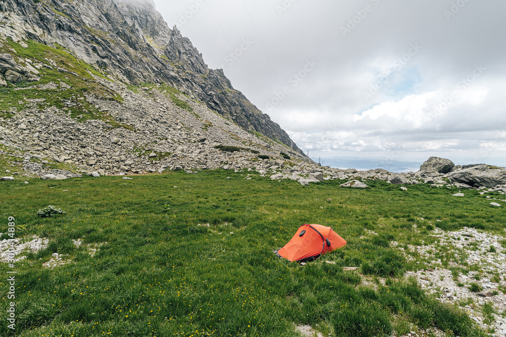 Red and orange tent pitched on a green meadow in high alpine mountain landscape. Outdoor overnight s