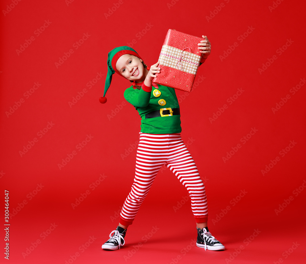 穿着圣诞精灵服装的快乐有趣的婴儿，红色背景上有礼物。